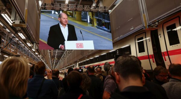 epa11068960 German Chancellor Olaf Scholz is seen on a screen as he speaks at the opening ceremony of the new Deutsche Bahn ICE4 express train plant in Cottbus, Germany, 11 January 2024. New ICE factory will help Deutsche Bahn's to increase the number of rapidly growing ICE 4 fleet and test new technologies as DB is planning to increase the number of long-distance passengers to 260 million per year by 2030.  EPA/FILIP SINGER
