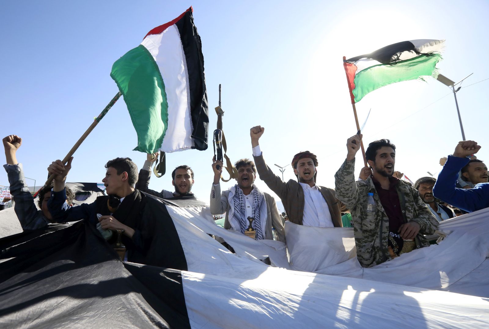 epa11121151 Houthi supporters wave Palestinian flags and shout slogans through gaps in a large-scale Palestinian flag during a protest against US-led strikes on Houthi positions, in Sana'a, Yemen, 02 February 2024. Thousands of Houthis supporters demonstrated in Sana'a to show solidarity with the Palestinian people and protest against US-led strikes on Houthi positions in Yemen. US and British forces have conducted strikes in response to Houthi missile and drone attacks on military and commercial vessels in the Red Sea, the Bab al-Mandab Strait, and the Gulf of Aden since November 2023. In January 2024, the US Department of State designated Yemen's Houthis as a 'Specially Designated Global Terrorist group' due to their increased attacks on shipping lanes. In December 2023, the US Department of Defense announced a multinational operation to safeguard trade and protect ships in the Red Sea in response to the escalation of Houthi attacks.  EPA/YAHYA ARHAB