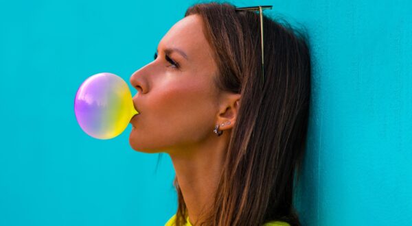 Portrait of young beautiful lady in yellow t-shirt standing isolated on turquoise background wall while blowing bubble with colourful chewing gum. High quality photo,Image: 549353114, License: Royalty-free, Restrictions: , Model Release: no, Credit line: Daria Kulkova / Alamy / Alamy / Profimedia