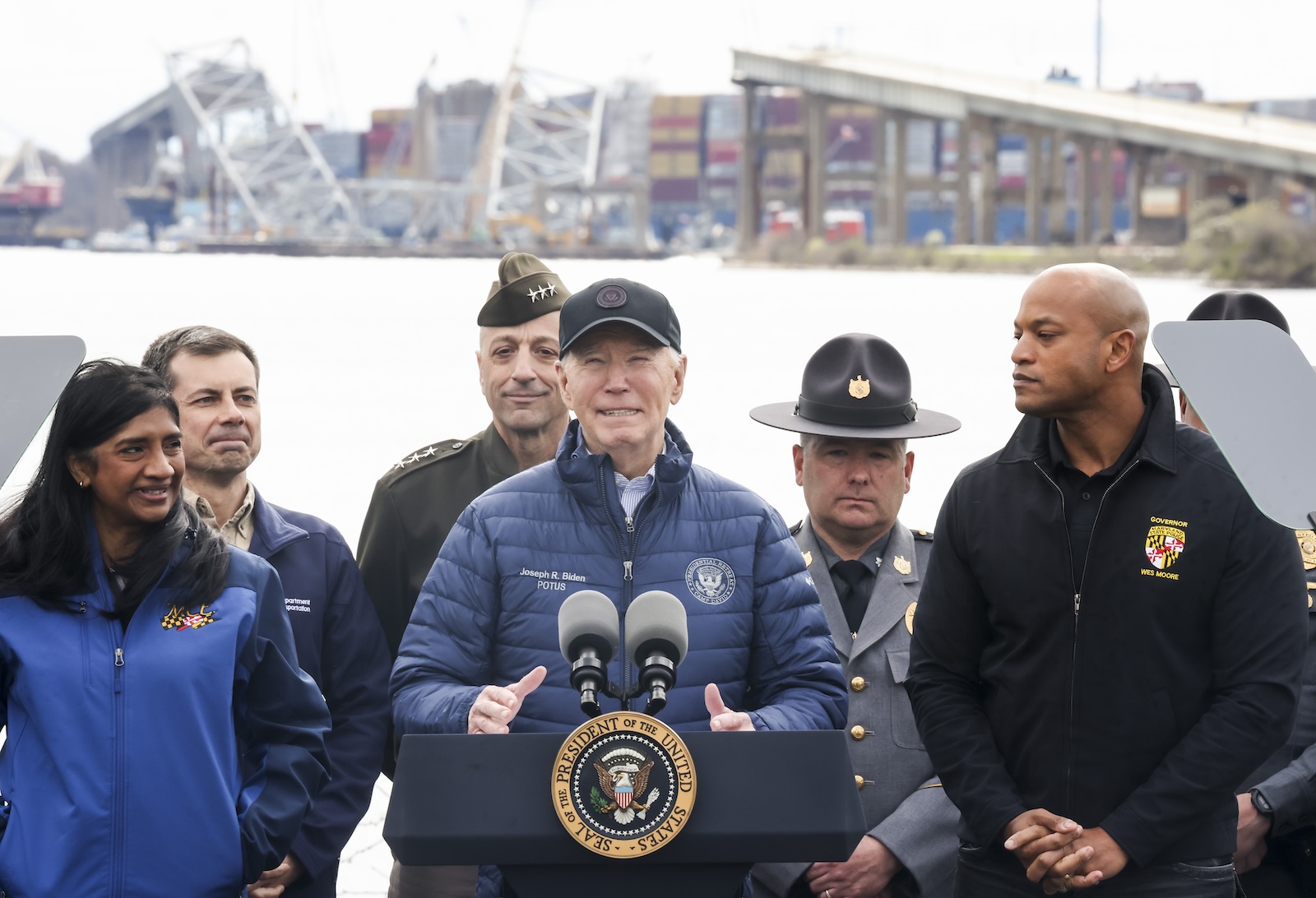 epa11261225 US President Joe Biden (C) delivers remarks near the wreckage of the Francis Scott Key Bridge, in the background, while standing with Maryland Governor Wes Moore (R), US Secretary of Transportation Pete Buttigieg (2-L), among others, in Dundalk, Maryland, USA, 05 April 2024. Biden delivered remarks on his administration's commitment to rebuilding and reopening the Port of Baltimore after the cargo vessel Dali struck the bridge on 26 March 2024.  EPA/MICHAEL REYNOLDS
