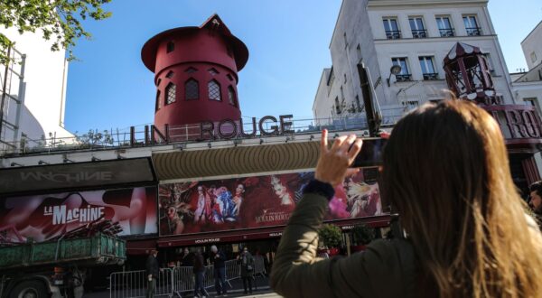 epa11299325 People stop to take photos of the facade of the Moulin Rouge without its wings in Paris, France, 25 April 2024. During the night of 24 to 25 April, the blades of the Moulin Rouge collapsed without causing any casualties, according to official sources.  EPA/Teresa Suarez