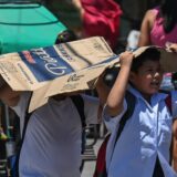Students use a cardboard to protect themselves from the sun during a hot day in Manila on April 2, 2024.  More than a hundred schools in the Philippine capital shut their classrooms on April 2, as the tropical heat hit 