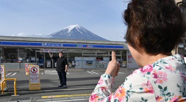 A person takes pictures of Mount Fuji from across the street of a convenience store, hours before the installation of a barrier to block the sight of Japan's Mount Fuji to deter badly behaved tourists, in the town of Fujikawaguchiko, Yamanashi prefecture on May 21, 2024. The plan to erect a large mesh barrier across the road from an Instagram-famous view of Mount Fuji made headlines last month when it was announced by officials fed up with what locals said were unending streams of mostly foreign visitors littering, trespassing and breaking traffic rules.,Image: 875012973, License: Rights-managed, Restrictions: , Model Release: no, Credit line: Kazuhiro NOGI / AFP / Profimedia